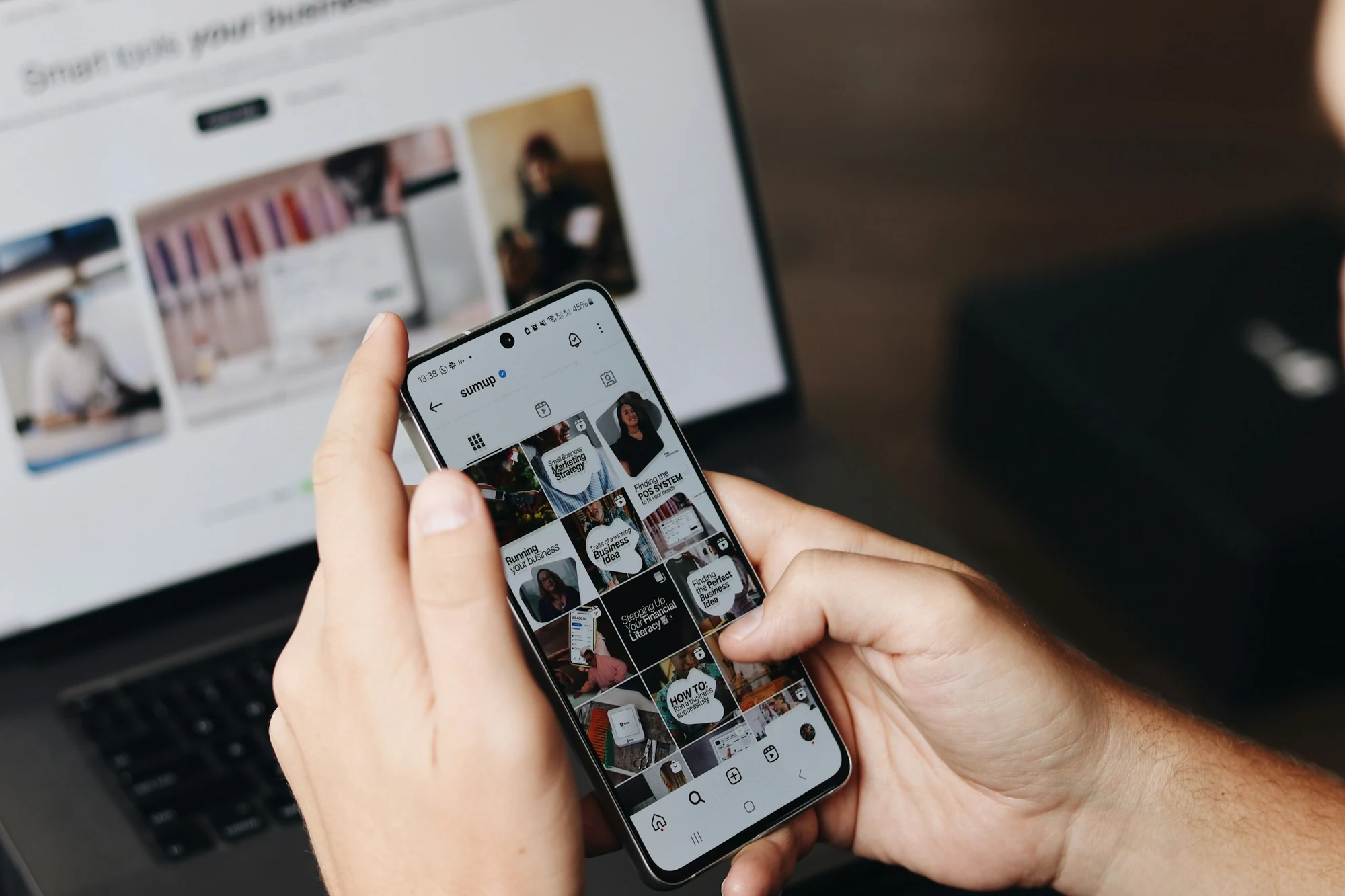 Hands editing social content on a phone beside a laptop